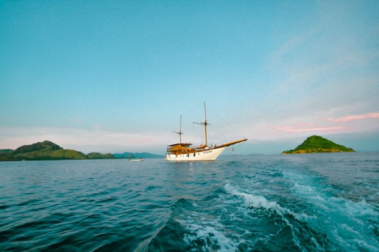 Adishree phinisi sailing near small islands with boat wake visible in foreground