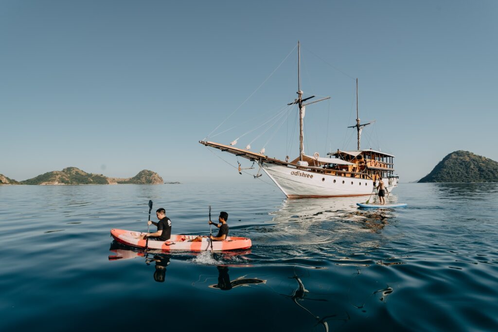 Two guests kayaking near the anchored Adishree phinisi with islands behind