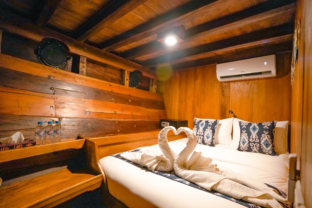 Cozy wood cabin bed aboard Adishree with patterned pillows and a swan towel display
