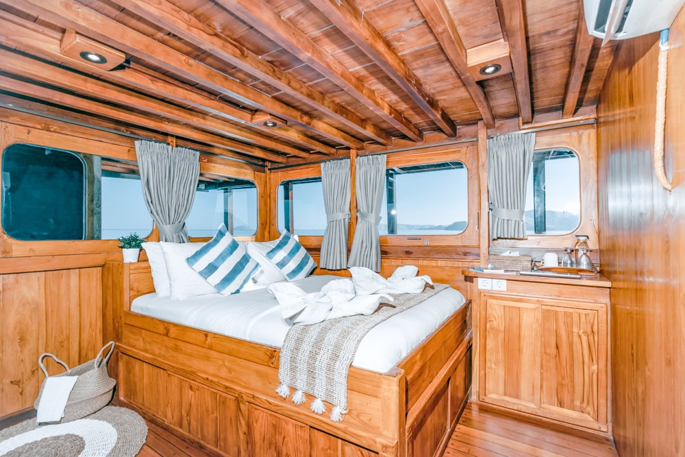 Wood-paneled bedroom aboard Adishree with striped pillows and an ocean-view window