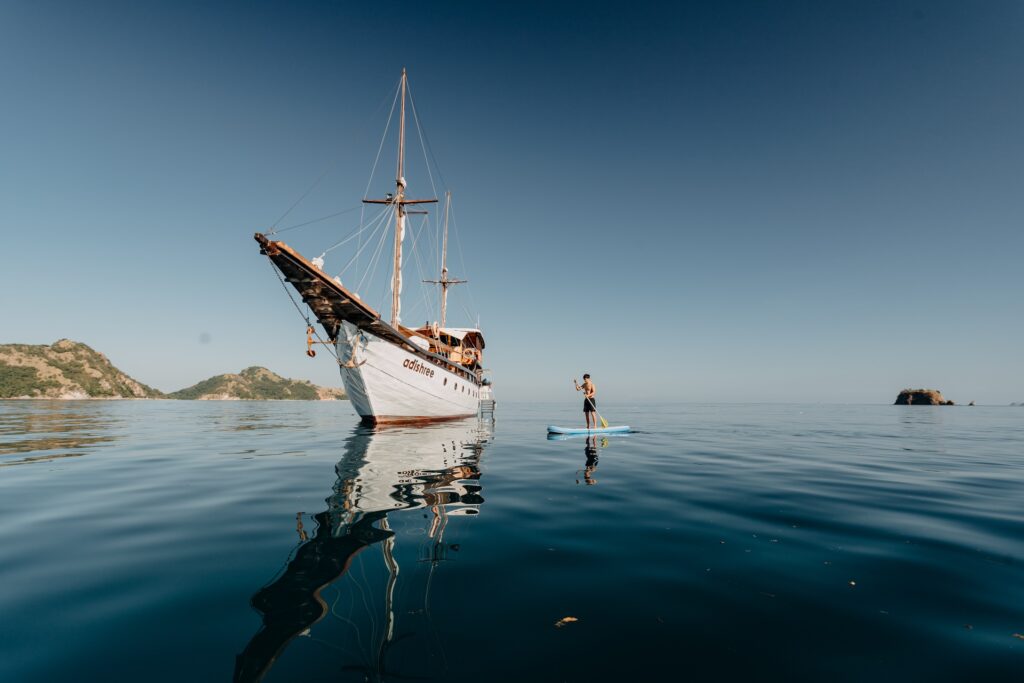 Adishree at anchor while a guest paddleboards nearby on flat calm water