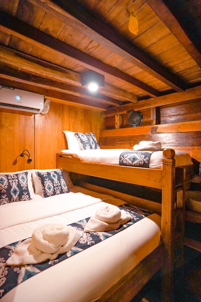 Triple bunk cabin with wood-paneled walls and neatly made twin beds