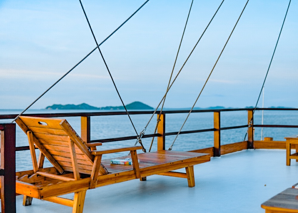 Wooden deck lounger facing distant islands beneath rigging ropes and lines