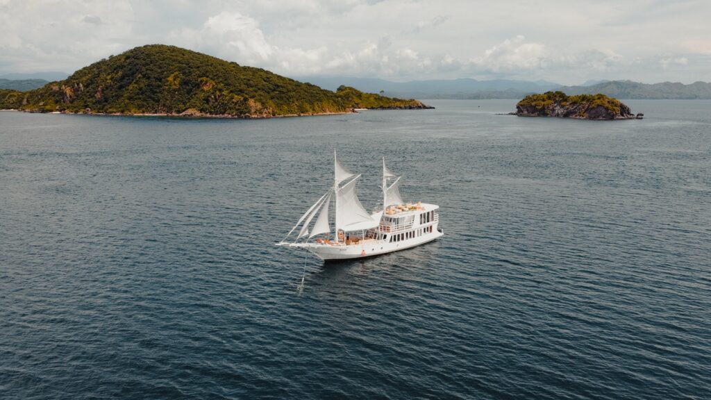 Akassa Cruise phinisi at anchor with sails furled near green islands