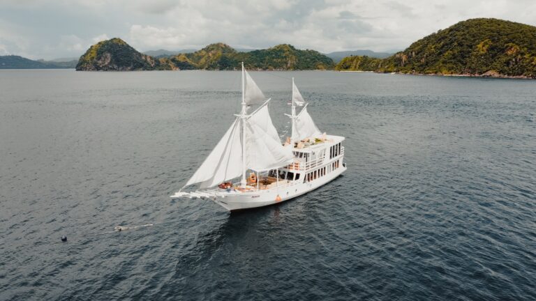 Akassa cruise komodo liveaboard phinisi sailing with sails raised past green islands