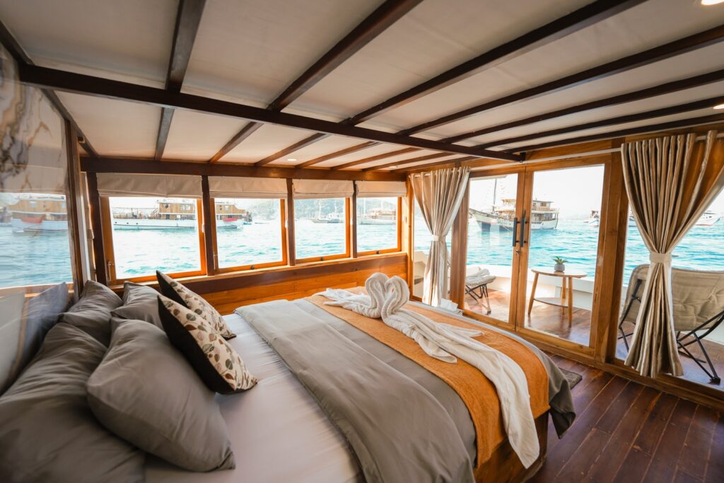 Akassa Cruise cabin bed with wraparound windows overlooking anchored boats in the harbor