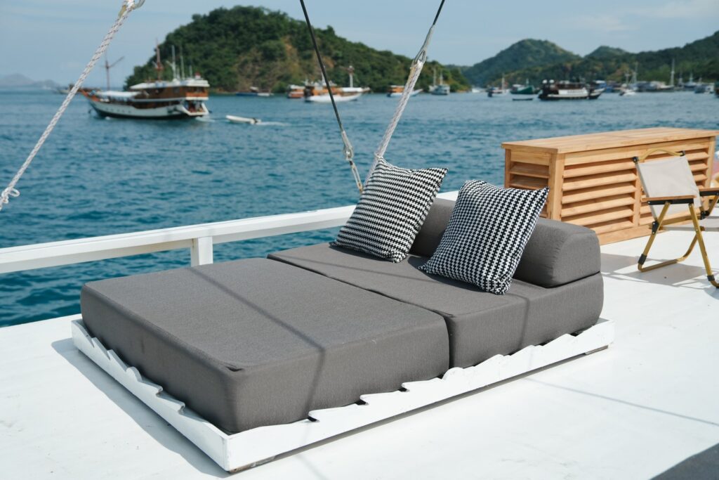 Grey cushioned sunbed on the top deck with striped pillows and a coastal view