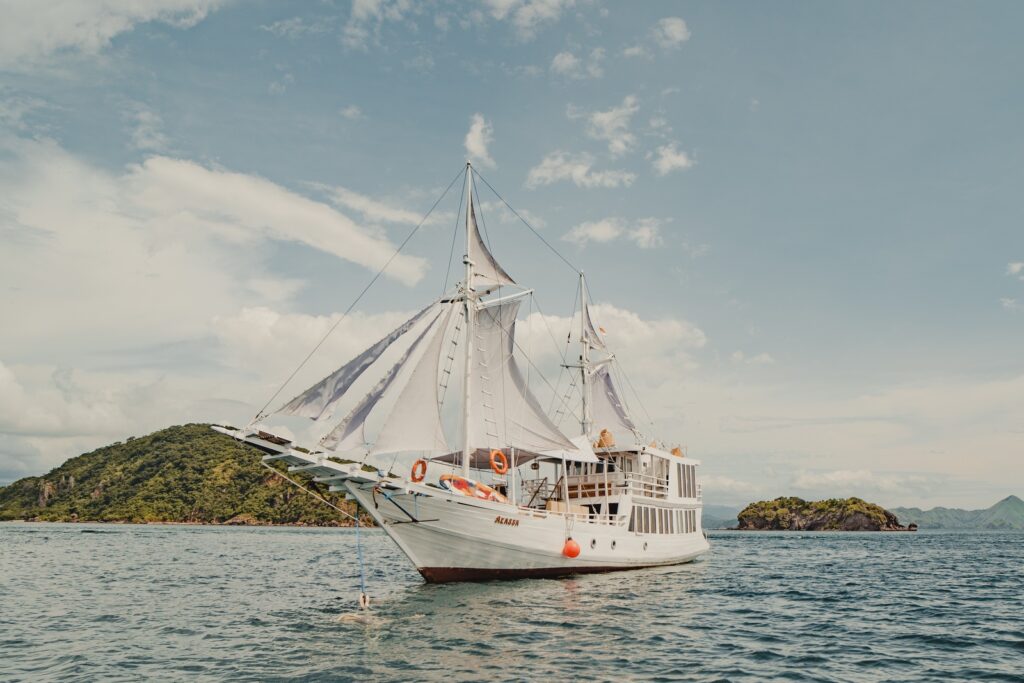 Akassa Cruise phinisi anchored with white sails unfurled near a green island