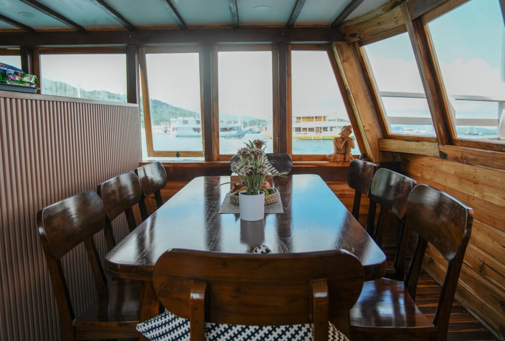 Wood dining table and chairs inside a cabin with large harbor-view windows