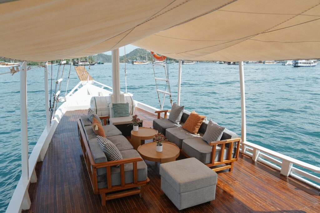 Shaded outdoor lounge with grey sofas and wooden tables on Akassa Cruise's front deck