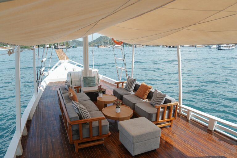 Shaded outdoor lounge with grey sofas and wooden tables on Akassa Cruise's front deck
