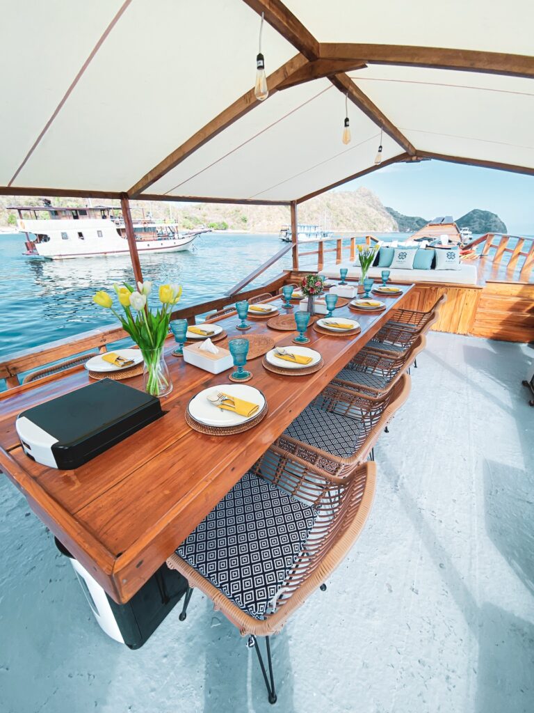 Wooden dining table set under a canopy with wicker chairs and a harbor view