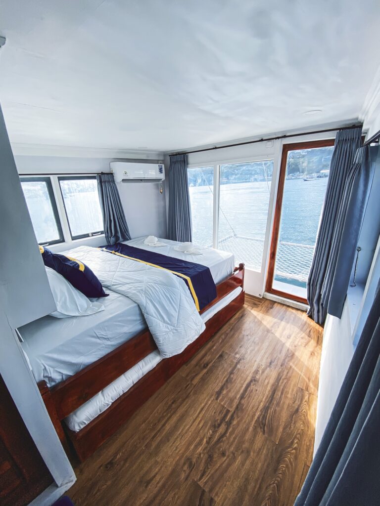 Cabin bed beside ocean-view windows with a folded navy towel accent