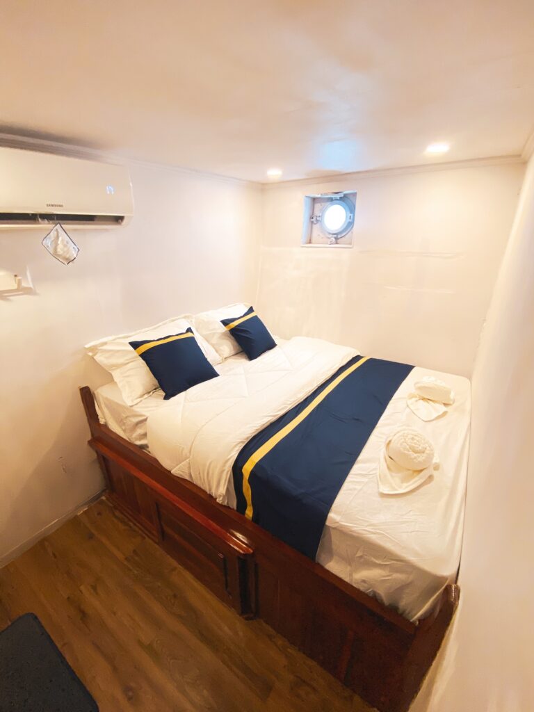 Amalfi cabin bed with a navy and gold runner beneath a small porthole window