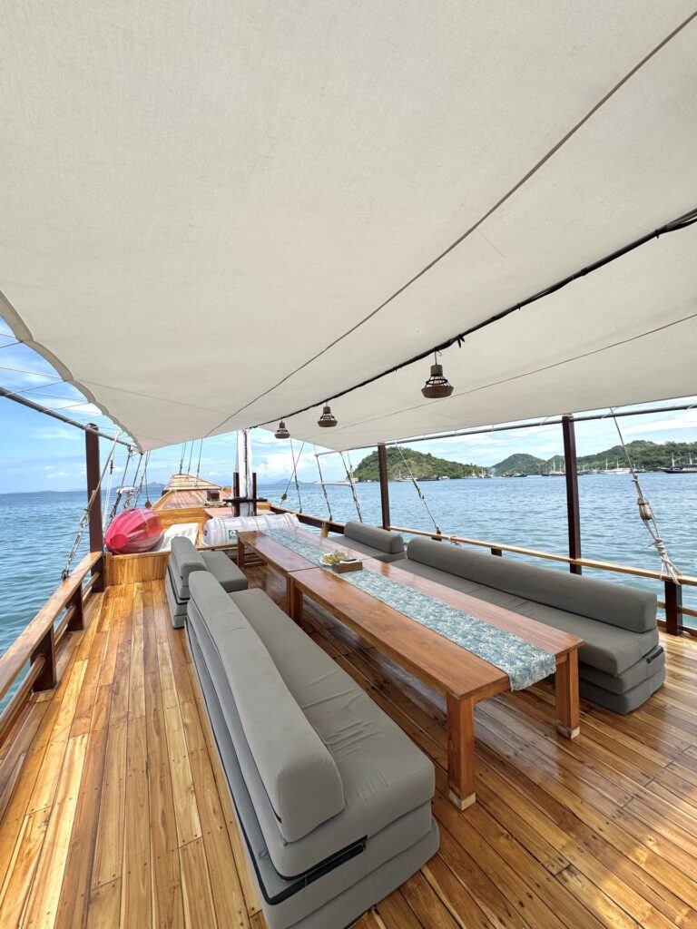 Shaded deck lounge with grey cushioned seating, a wooden table and string lights