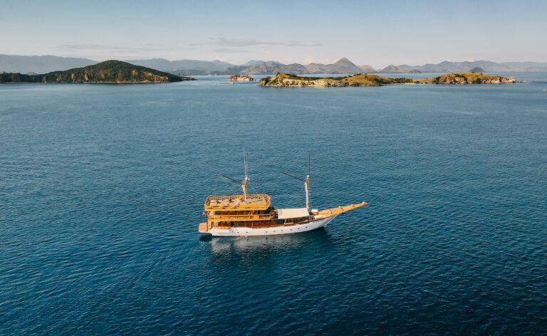 Andamari komodo liveaboard sailing past a green island in warm light