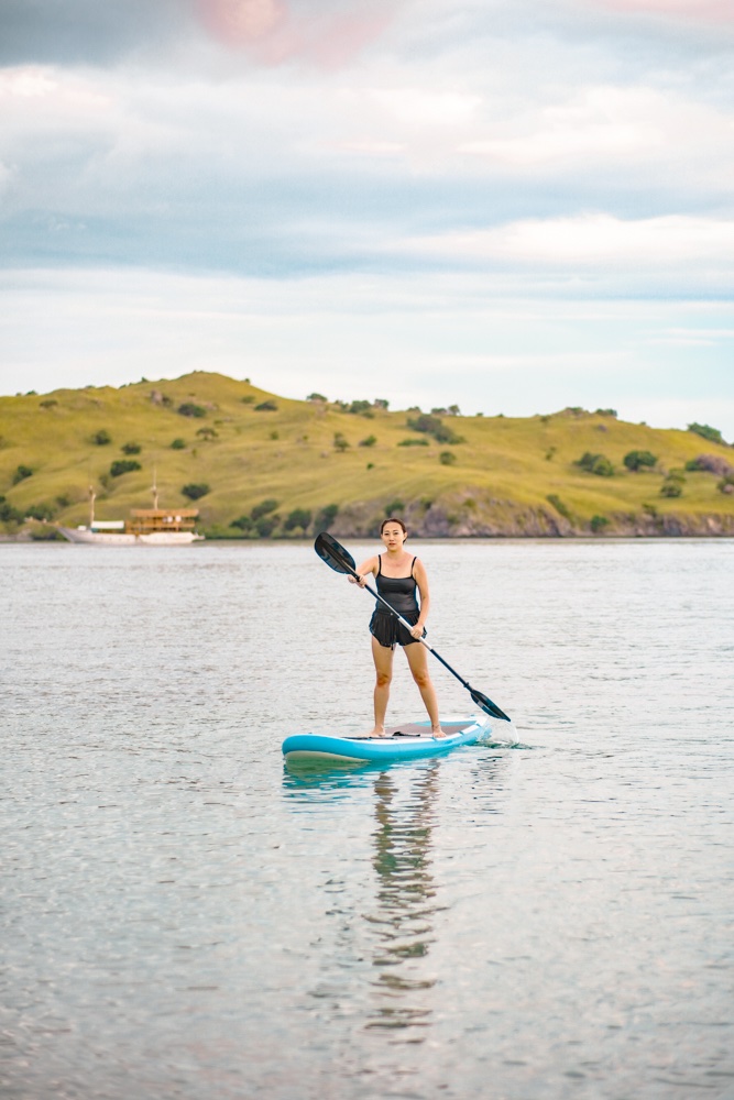 Guest paddleboarding near a green island with the boat visible in the distance