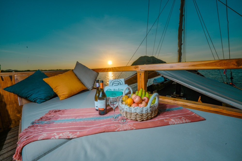 Cushioned deck lounge at sunset with a fruit basket and bottle of wine