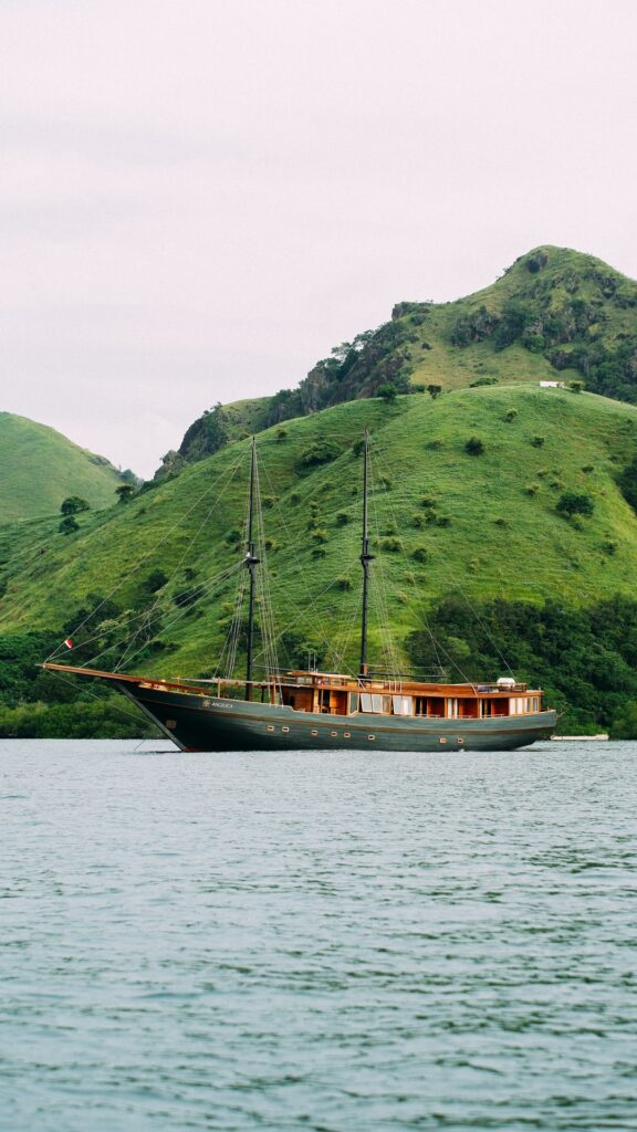 Angelica anchored close to a steep green hillside under grey skies
