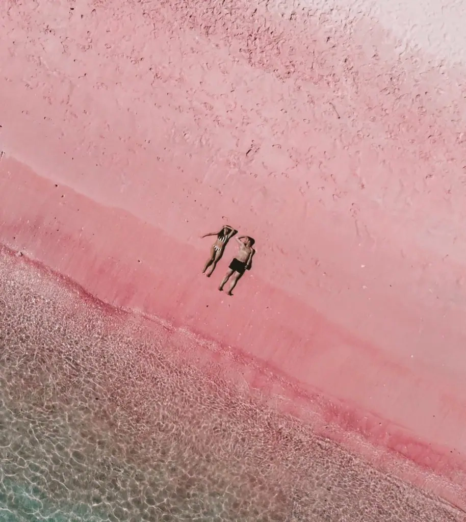 Overhead aerial photograph of two guests relaxing on the famous pink sand shoreline with crystal-clear shallow water during an Anne Bonny luxury yacht escape in Labuan Bajo.