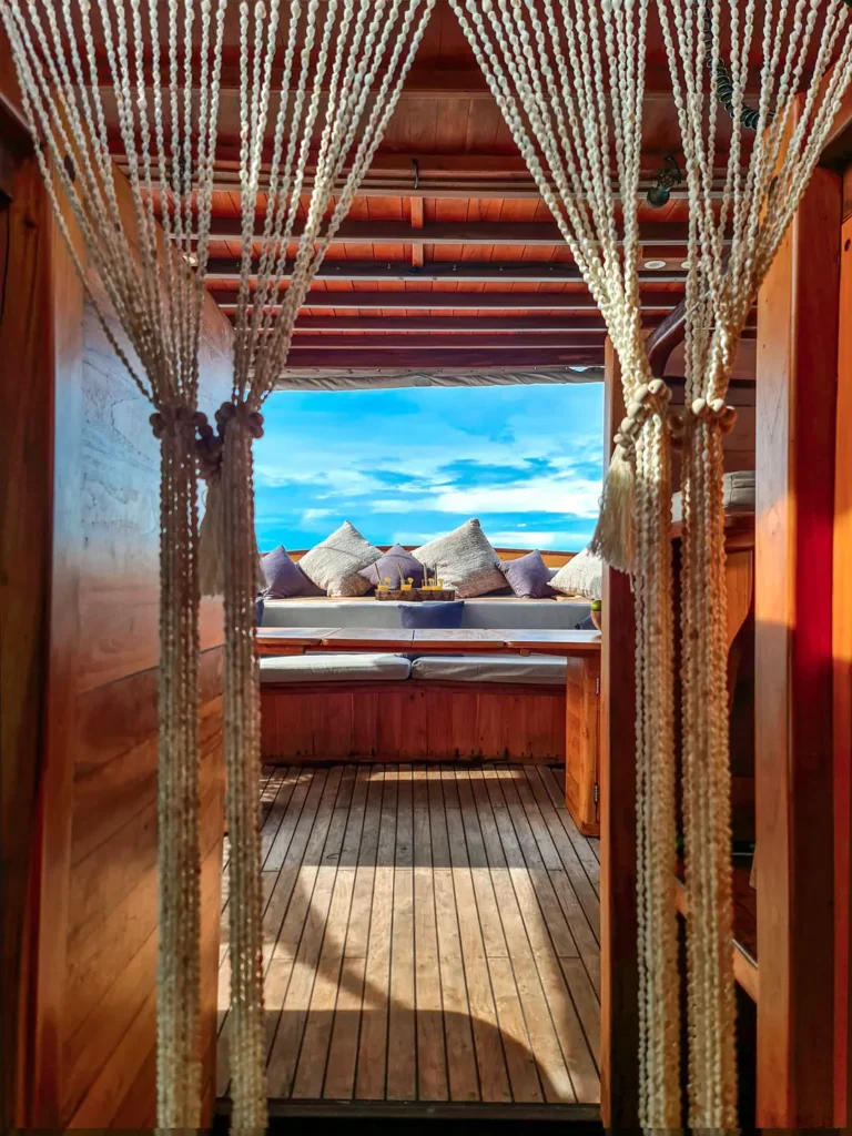 Warm wooden interior corridor leading toward an open-air lounge deck with ocean views aboard the Anne Bonny luxury Phinisi in Raja Ampat.