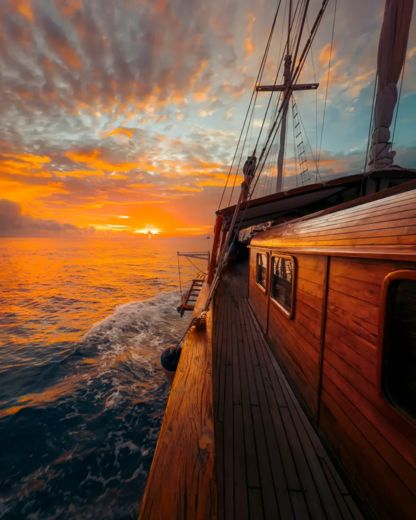 Warm sunset view from the Anne Bonny luxury Phinisi deck while cruising through calm ocean waters under vibrant tropical skies.