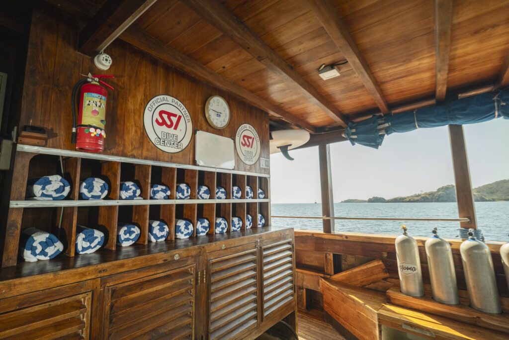 Organized towel station and scuba setup area aboard Cajoma V dive liveaboard featuring polished teak cabinetry and dedicated diver preparation space.