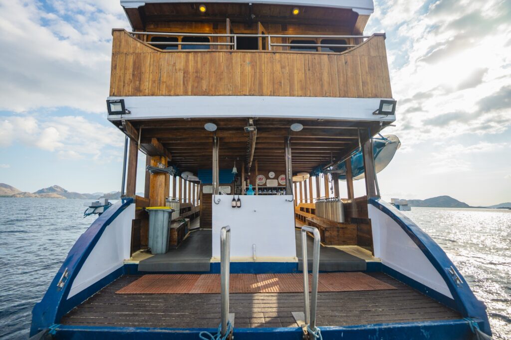 Rear boarding and dive platform aboard Cajoma V liveaboard featuring wide ocean access, polished teak structures, and a spacious lower deck designed for diving activities in Komodo Islands.
