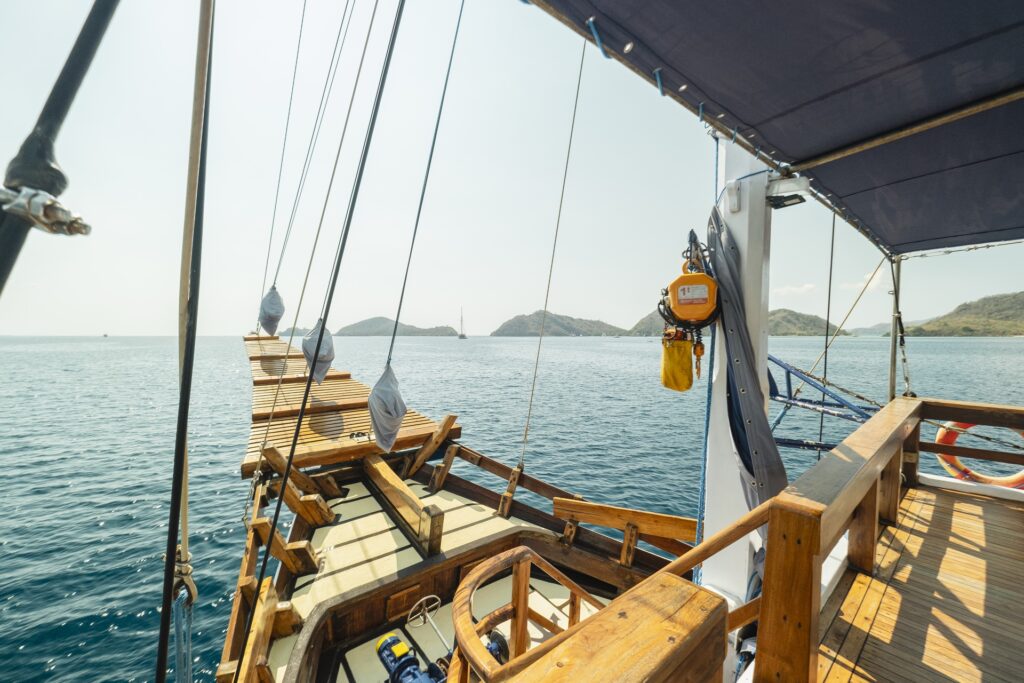 Forward deck walkway aboard Cajoma V liveaboard overlooking calm turquoise waters and scattered tropical islands under clear afternoon skies.