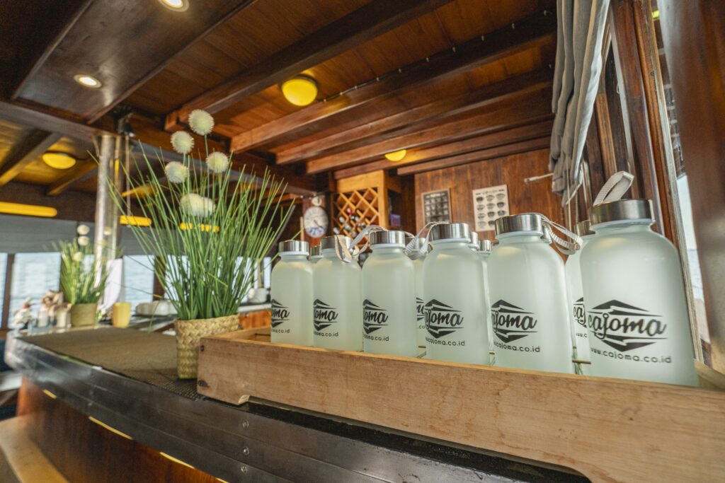 Reusable Cajoma V water bottles displayed inside the onboard lounge area, highlighting sustainable amenities and polished wooden interiors.