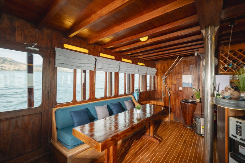 Intimate indoor dining corner aboard Cajoma V liveaboard with ocean-facing windows, polished wooden finishes, and comfortable cushioned seating.