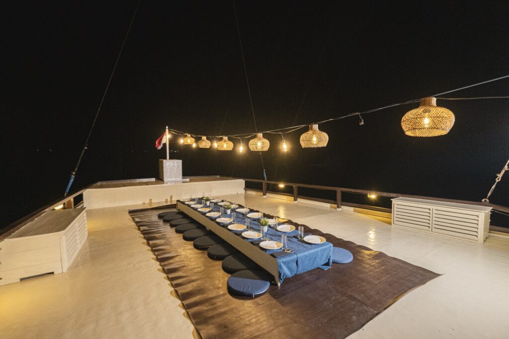 Elegant rooftop dining experience aboard Cajoma V luxury liveaboard illuminated by hanging lanterns and ambient evening lighting beneath the night sky.