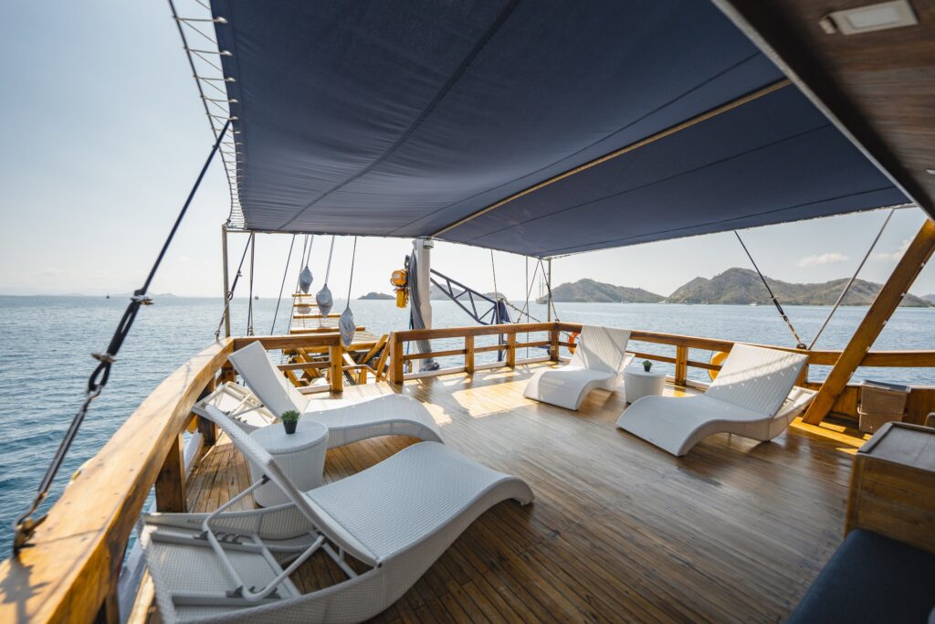 Sunlight filters across the shaded relaxation deck of Cajoma V private charter, where white woven loungers and teak flooring create an inviting open-air lounge overlooking tropical islands.