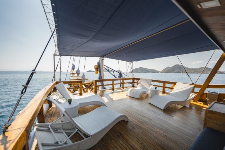 Sunlight filters across the shaded relaxation deck of Cajoma V private charter, where white woven loungers and teak flooring create an inviting open-air lounge overlooking tropical islands.