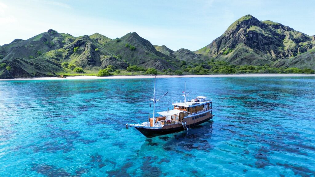 Capt Octopus anchored over turquoise water near a beach and green mountains