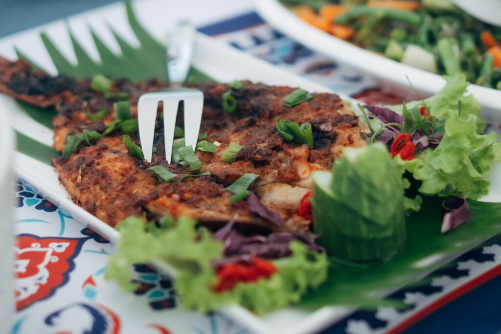 Grilled fish dish garnished with herbs and vegetables on a patterned plate