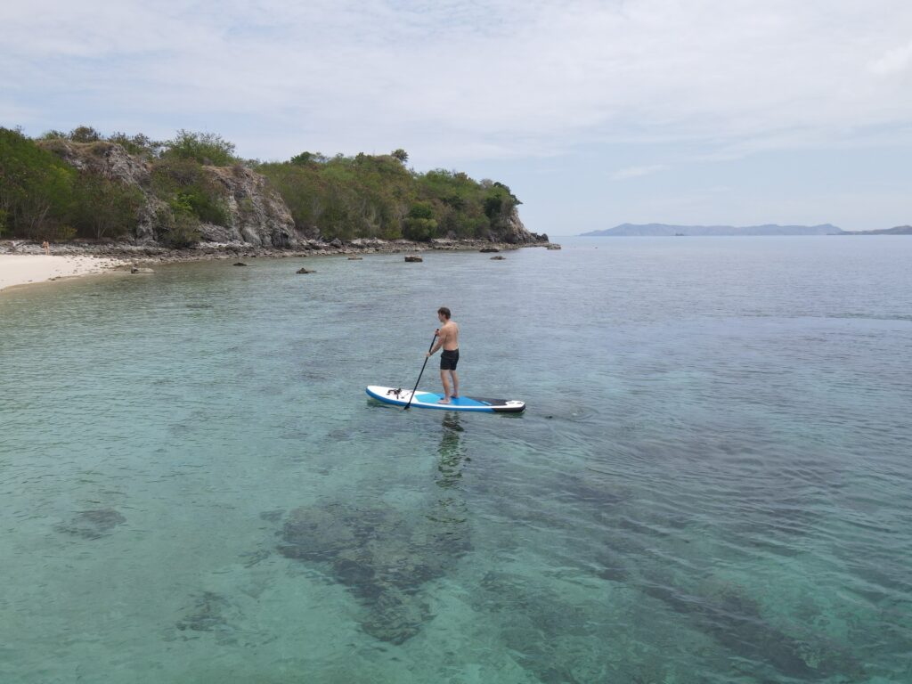 A guest paddleboarding over clear shallow water near a rocky coastline