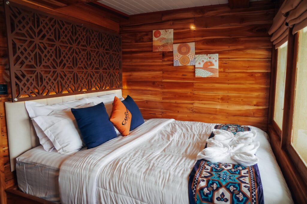 Owners suite bed with a carved wooden headboard and navy and orange pillows