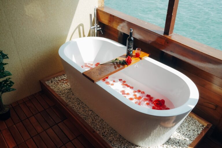 Freestanding bathtub scattered with rose petals beside a private balcony window