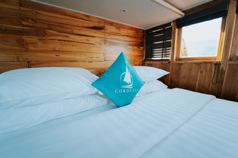 Cordelia phinisi bed with white linens and a teal branded pillow