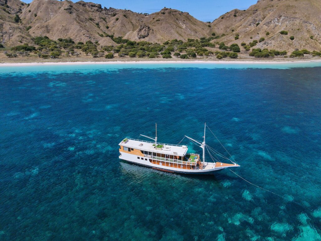 Aerial view of the Dinara anchored near a white sand beach and green hills