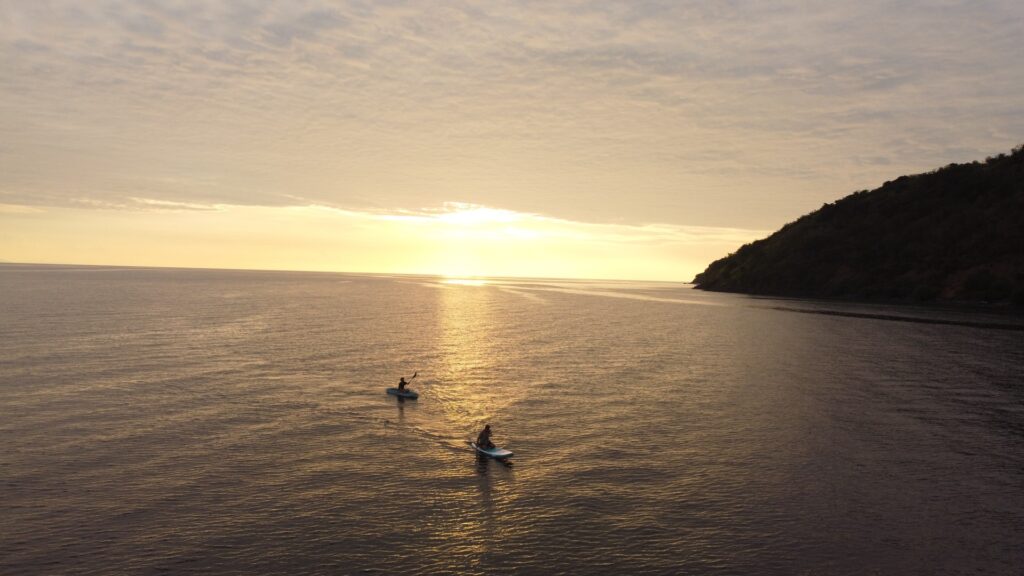 Two guests kayaking on calm water during a golden sunset near a hillside