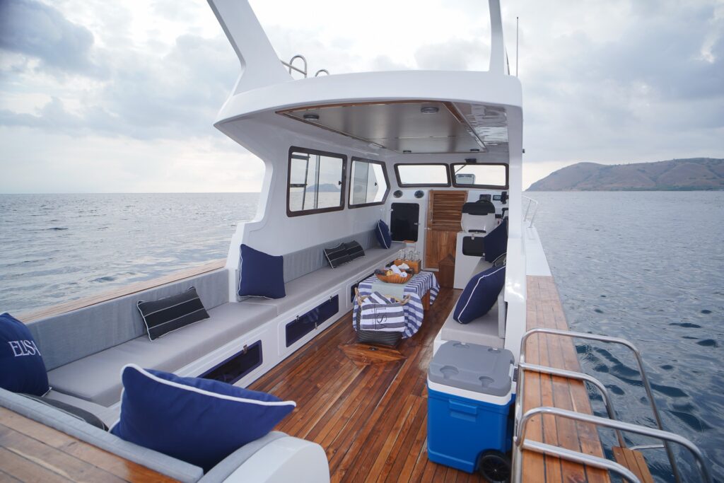 Boat deck with teak flooring, a blue cooler box and striped cushions