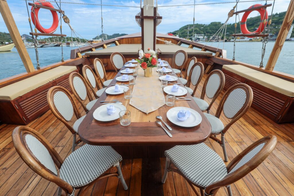 Outdoor dining table with woven chairs, white plates and a floral centerpiece