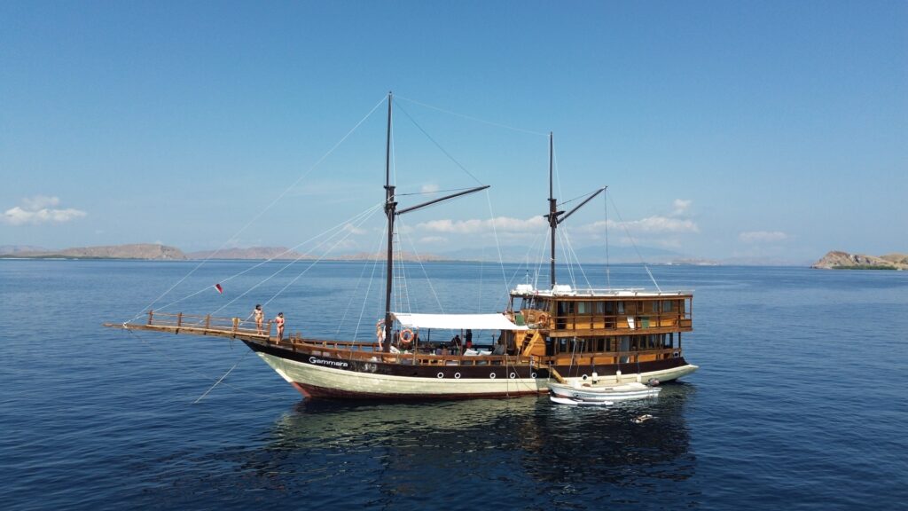 Gammara phinisi anchored beside its tender, masts up, islands behind