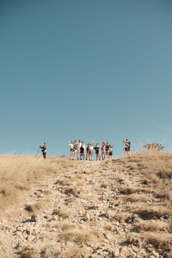 A group of guests hiking up a dry grassy hilltop trail under clear sky