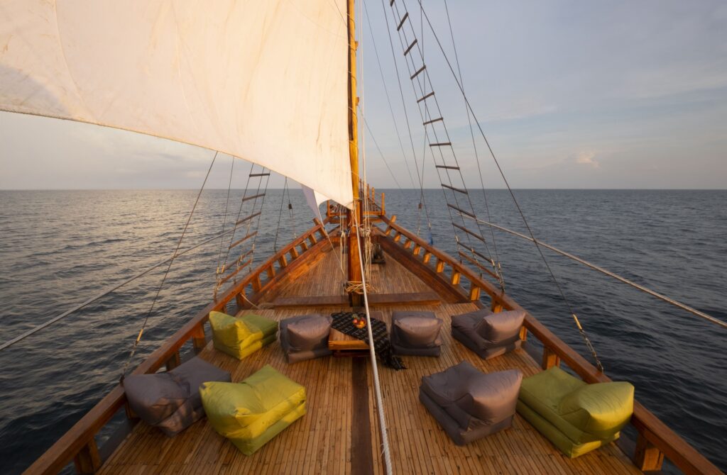 Bow deck of the Gammara with cushioned seating and one sail raised at dusk