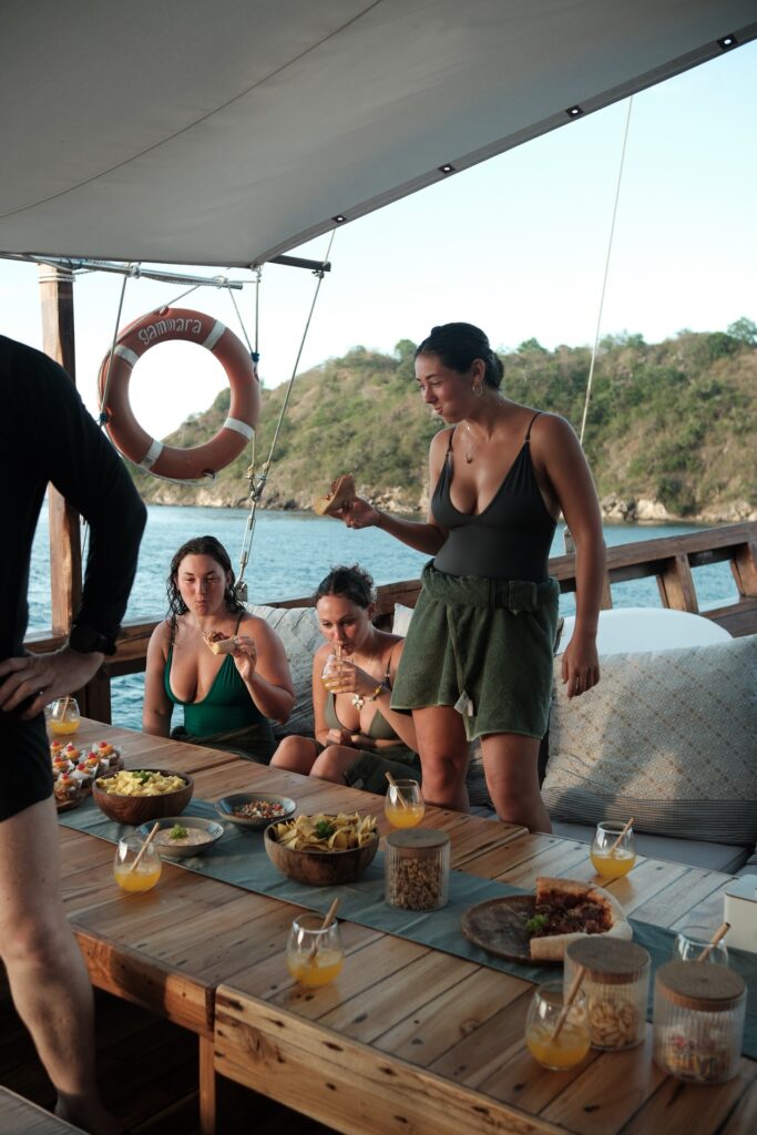 Guests laughing over a deck lunch spread of tropical fruit and drinks