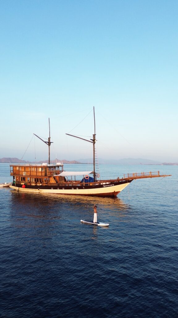 A paddleboarder near the anchored Gammara, sails furled against a clear sky