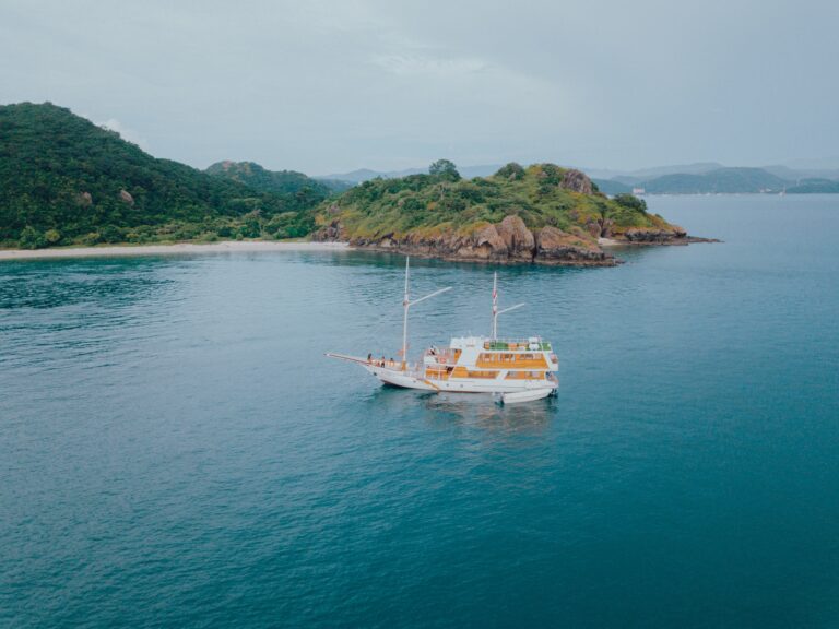 Aerial view of the Gandiva anchored near a sandy beach and green hills